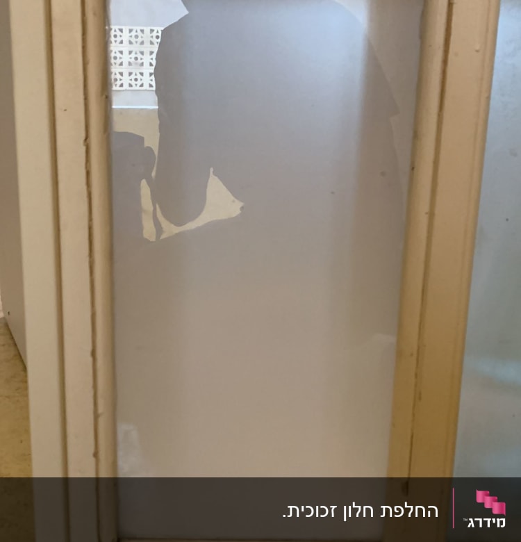 צללית אדם מאחורי זכוכית חלבית במסגרת עץ